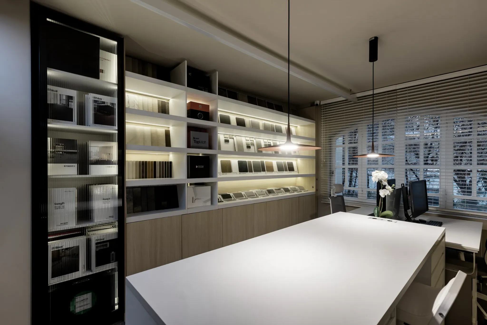 Studio meeting table beside illuminated material and book shelves.